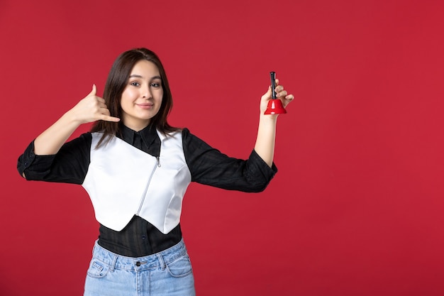 vue de face jeune serveuse en uniforme tenant une petite cloche sur le fond rouge femme dîner travail soir travailleur beauté emploi restaurant