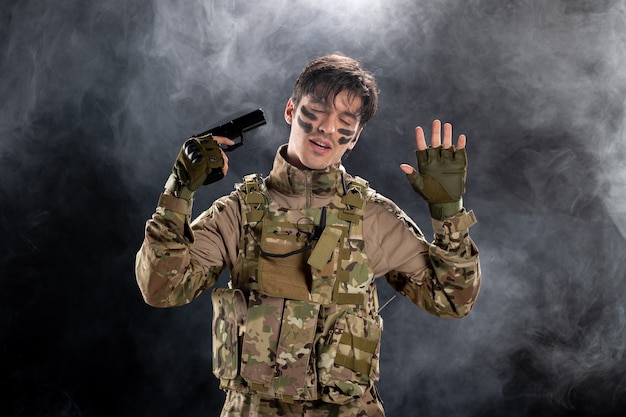 Vue de face d'un jeune soldat en uniforme avec un mur fumé noir