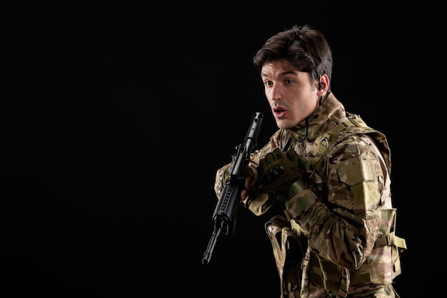 Vue de face jeune soldat en uniforme sur le mur noir