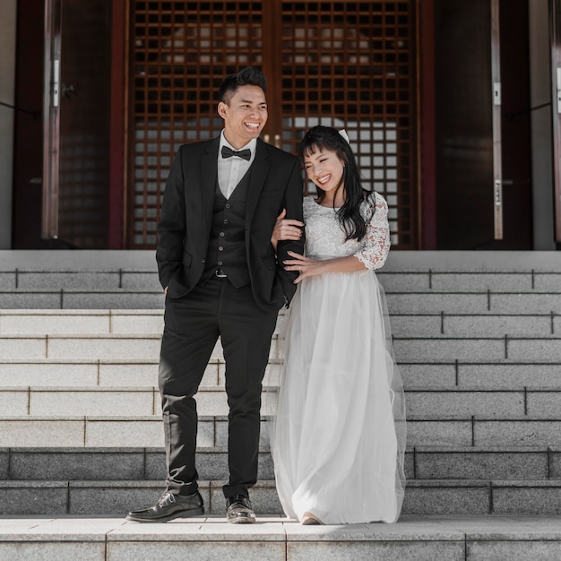 Photo vue de face des jeunes mariés posant ensemble sur les marches