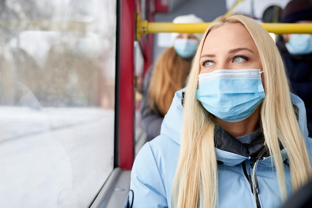 Vue de face d'une jolie femme portant un masque de protection et une veste bleue assise avec des passagers derrière