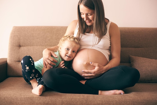 Vue de face d'une jolie fille assise sur un canapé avec une mère enceinte