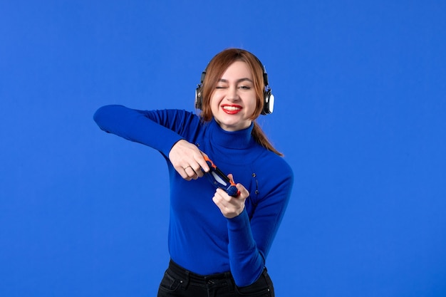 vue de face joueur féminin avec un casque et une manette de jeu jouant à un jeu vidéo sur fond bleu canapé jeune fille gagnant joueur vidéo adulte virtuel