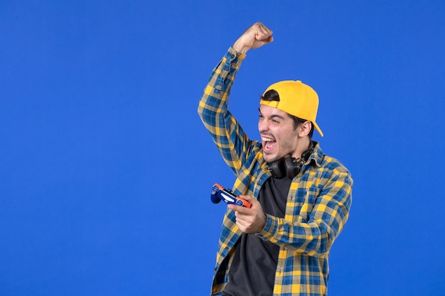 Vue de face d'un joueur masculin acclamant avec une manette de jeu jouant à un jeu vidéo sur un mur bleu