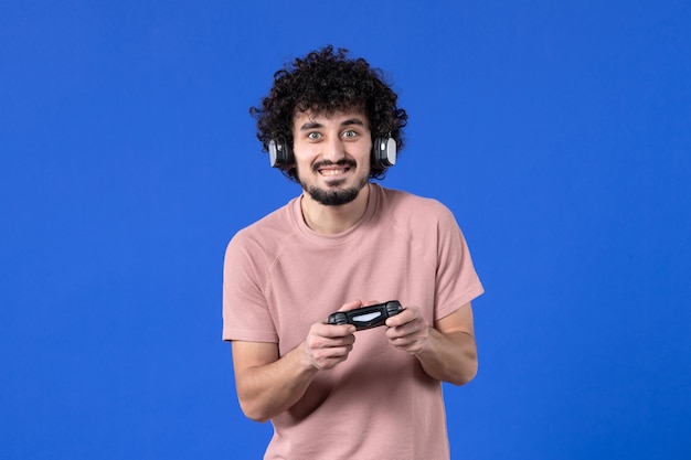 vue de face joueur masculin avec manette de jeu et casque jouant à un jeu vidéo sur fond bleu vidéo virtuelle football adolescent adulte gagnant jeunes joueurs de joie