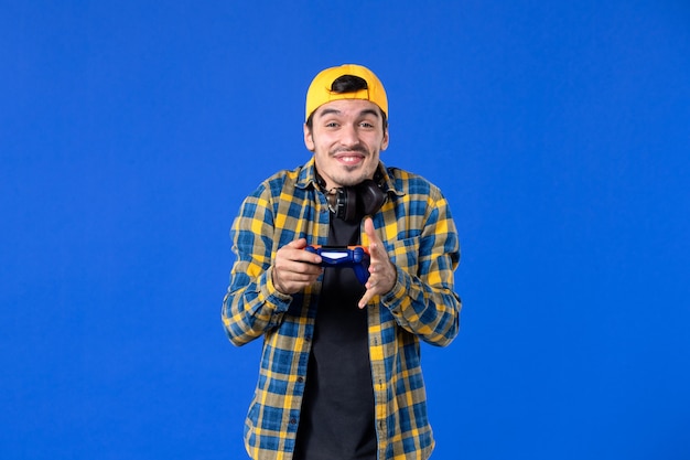 Vue de face d'un joueur masculin avec une manette de jeu jouant à un jeu vidéo sur un mur bleu