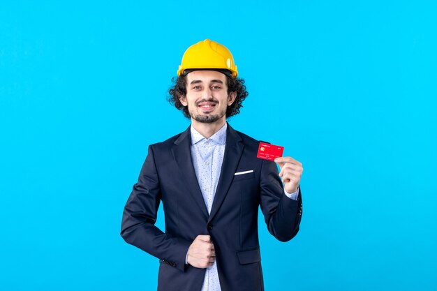 Vue de face mâle builder holding bank card sur fond bleu job business architecture ingénieur constructeur couleur du bâtiment