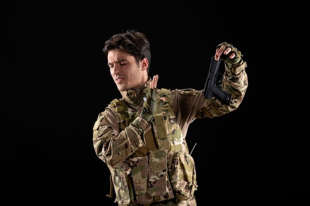 Vue de face d'un militaire en uniforme avec un mur noir de pistolet noir
