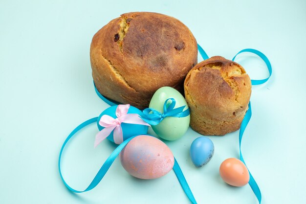 Photo vue de face des oeufs de pâques colorés avec une délicieuse cuisson sur une surface bleue ornée de vacances de pâques ethniques colorées printemps multi