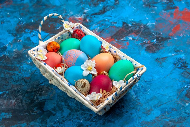 vue de face des oeufs de pâques colorés à l'intérieur d'une jolie boîte sur une surface bleue