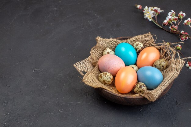 Vue de face des oeufs de pâques colorés à l'intérieur de la plaque sur fond sombre couleur printemps concept de vacances orné de Pâques coloré