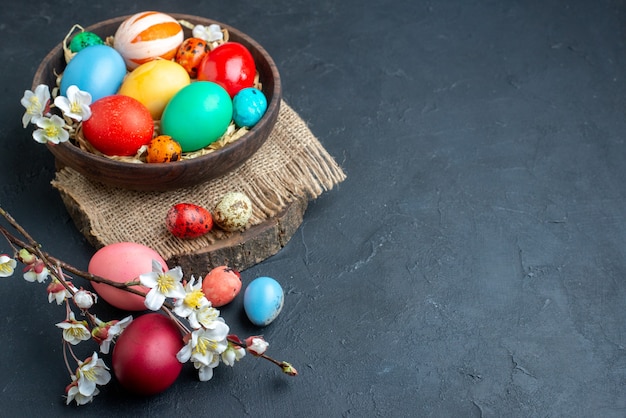 Vue de face des oeufs de pâques colorés à l'intérieur de la plaque avec de la paille sur une surface sombre ornée de vacances colorées groupe concept multi couleurs printemps