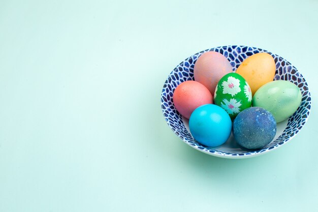 Vue de face des oeufs de pâques colorés à l'intérieur de la plaque sur la surface bleue printemps orné de couleurs ethniques multicolores