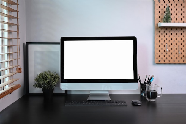 Vue de face de l'ordinateur avec une plante d'intérieur de cadre photo d'affichage vide et une tasse de café sur un tableau noir