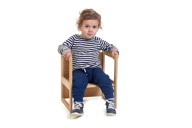 Photo vue de face d'un petit garçon assis sur une chaise et regardant la caméra sur fond blanc