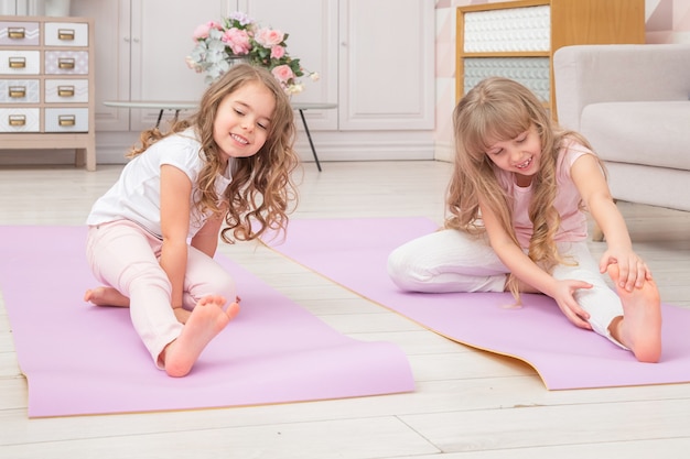 Vue de face pleine longueur souriante mignonnes petites filles d'âge préscolaire ludiques assis sur un tapis de yoga faire divers exercices.