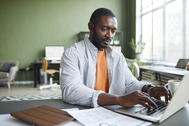 Vue de face portrait d'un homme d'affaires noir adulte travaillant au bureau à domicile et utilisant un espace de copie pour ordinateur portable