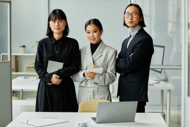 Vue de face portrait de trois hommes d'affaires asiatiques regardant la caméra tout en se tenant au bureau