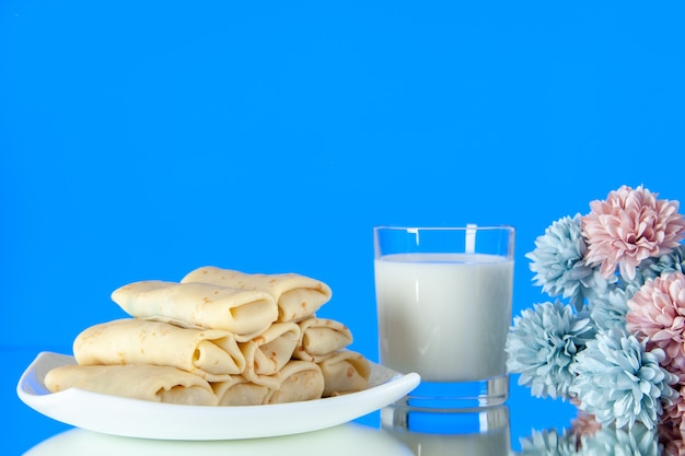 vue de face roulé des crêpes sucrées avec un verre de lait sur un fond bleu repas petit déjeuner nourriture matin sucre fleur couleur gâteau