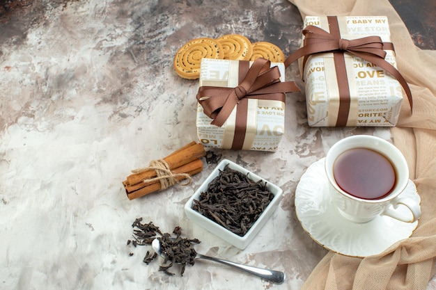 Vue de face tasse de thé avec des cadeaux et des biscuits sur fond clair goodie couleur gâteau sucré cadeau de vacances rouge amour saint valentin couple