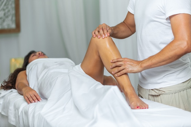 Vue de face d'un thérapeute faisant un massage des jambes et des genoux à une femme dans un salon de spa. Notion de spa.