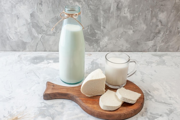 Photo vue de face tranches de fromage blanc tasse de lait sur une planche à découper bouteille de lait sur table