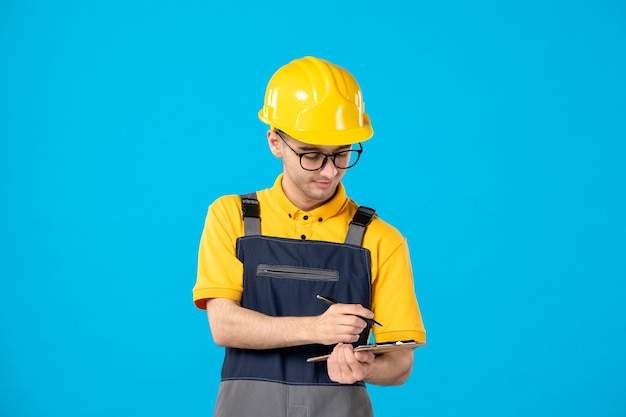 Vue de face travailleur masculin en uniforme jaune en prenant des notes sur le bleu