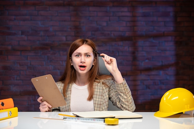 Vue de face travailleuse sur chantier assis derrière une table avec des documents emploi agenda d'entreprise plan manager ingénieur planificateur de projet business