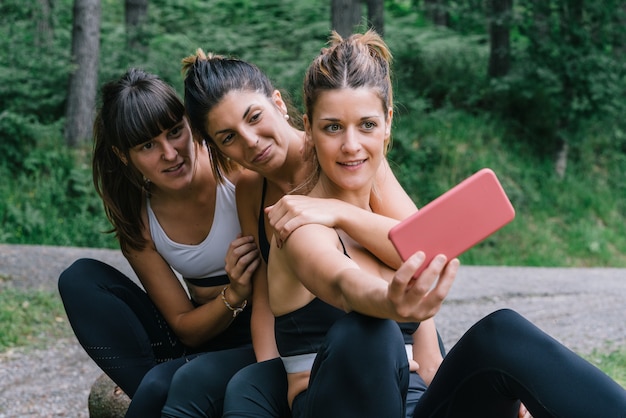 Vue de face de trois belles femmes sportives heureux faisant une vidéo ou photo selfie après une course dans une forêt verte