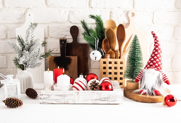Vue de face d'ustensiles de cuisine en bois écologiques et de décorations de Noël dans une boîte en bois sur une table en bois blanche contre un mur de briques