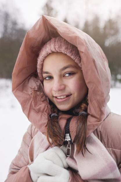 Vue de face verticale portrait d'une jolie fille portant une veste rose et souriant à la caméra tout en profitant d'une promenade à l'extérieur en hiver