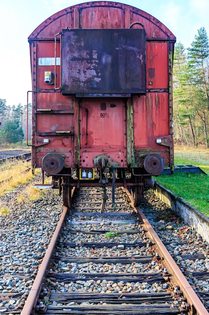 Photo vue de face d'un wagon de marchandises en métal rouge rouillé sur des voies ferrées désaffectées à l'ancienne gare, l'accouplement arrête les arbres en arrière-plan journée d'automne ensoleillée avec un ciel bleu dans le limbourg en belgique