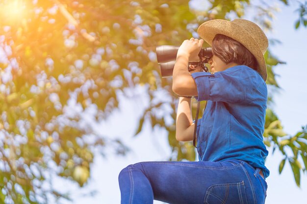 Photo vue à faible angle d'une adolescente regardant à travers des jumelles contre les arbres