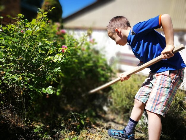 Vue à faible angle d'un garçon tenant un bâton alors qu'il se tient sur le terrain dans la cour arrière