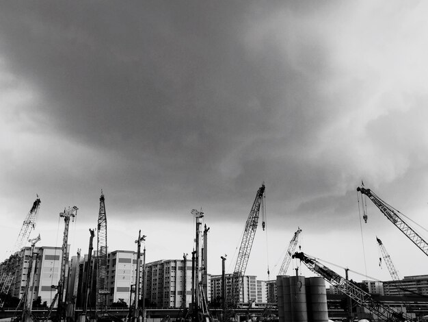 Vue à faible angle des grues avec des bâtiments contre un ciel nuageux