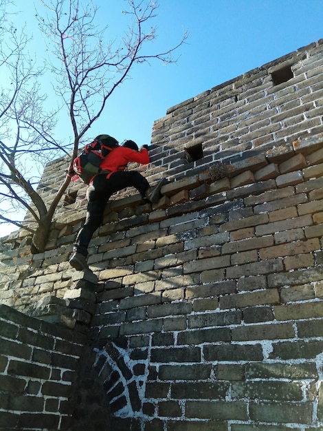 Photo vue à faible angle d'un homme adulte en train d'escalader un mur de briques contre le ciel bleu