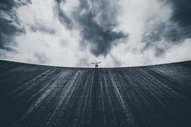 Vue à faible angle d'un homme avec les bras tendus debout sur le mur contre un ciel nuageux
