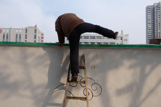 Vue à faible angle d'un homme grimpant sur le mur à l'aide d'une échelle