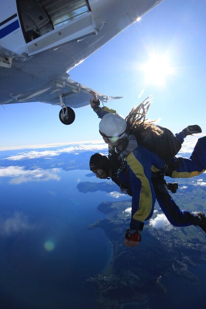 Photo vue à faible angle d'hommes faisant du parachutisme d'un avion volant au-dessus de la mer contre le ciel