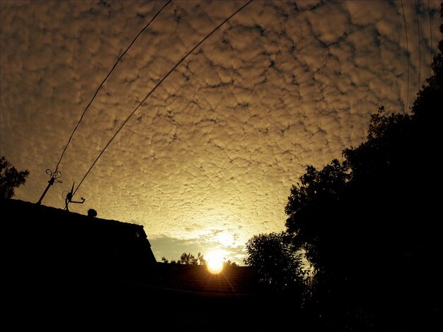 Photo vue à faible angle de maisons et d'arbres en silhouette contre un ciel nuageux au coucher du soleil