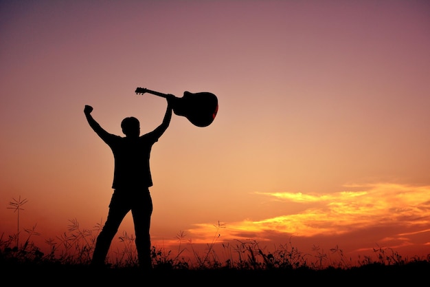 Vue à faible angle de la silhouette d'un homme avec les bras levés tenant une guitare contre le ciel