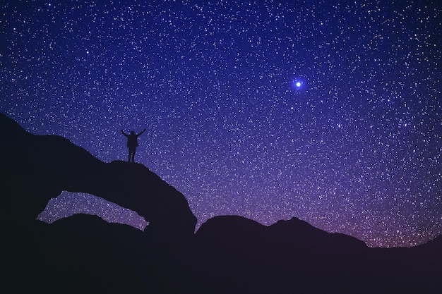 Photo vue à faible angle de la silhouette d'une personne debout sur une formation rocheuse contre un champ d'étoiles dans le ciel la nuit