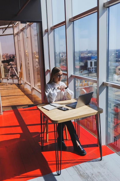 Vue d'une femme concentrée en tenue décontractée tapant sur un netbook tout en travaillant sur un nouveau projet assis à table dans un espace de travail moderne