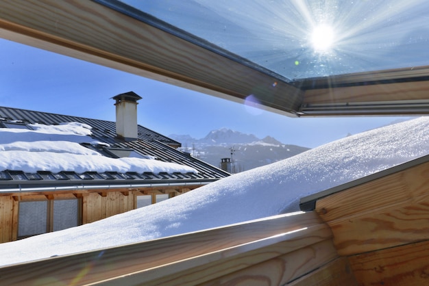 Vue d'une fenêtre s'ouvrant sur un toit recouvert de neige dans un chalet alpin