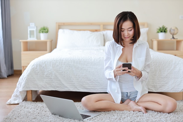 Vue frontale, de, asiatique, indépendant, femme asiatique, dans, chemise blanche, travailler ordinateur, et, téléphone portable, dans, chambre à coucher, à, sourire heureux