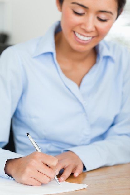 Vue frontale d&#39;une jolie femme écrivant sur une feuille de papier en position assise