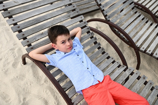 Vue grand angle d'un adolescent heureux allongé sur une chaise longue en bois. Beau gosse reposant sur la chaise longue pendant les vacances d'été à la campagne. Enfants en vacances