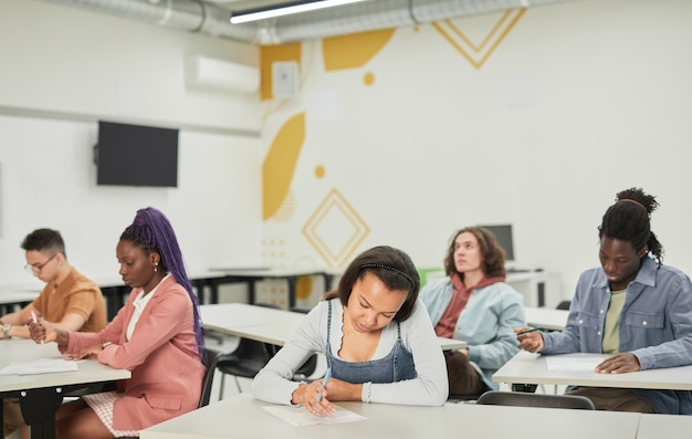 Vue grand angle sur divers groupes d'étudiants assis à des bureaux en classe d'école en mettant l'accent sur une jeune femme afro-américaine devant, espace pour copie