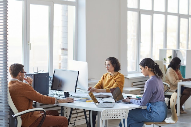 Vue grand angle sur diverses équipes de développement de logiciels utilisant des ordinateurs sur le lieu de travail dans un intérieur de bureau blanc, espace de copie