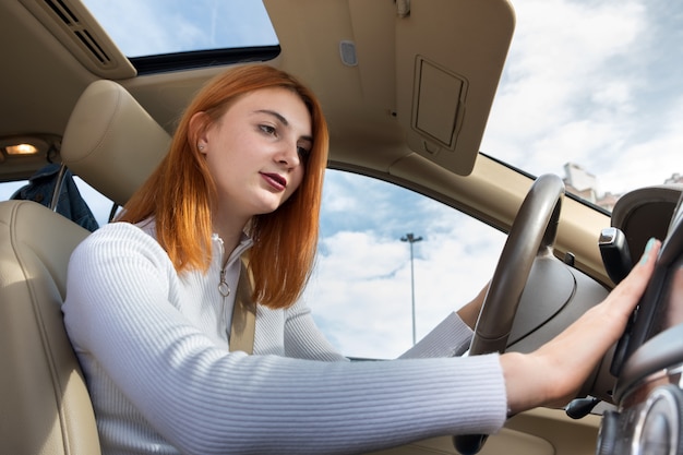 Vue grand angle du jeune femme rousse chauffeur attaché par la ceinture de sécurité au volant d'une voiture réglage du chauffage.